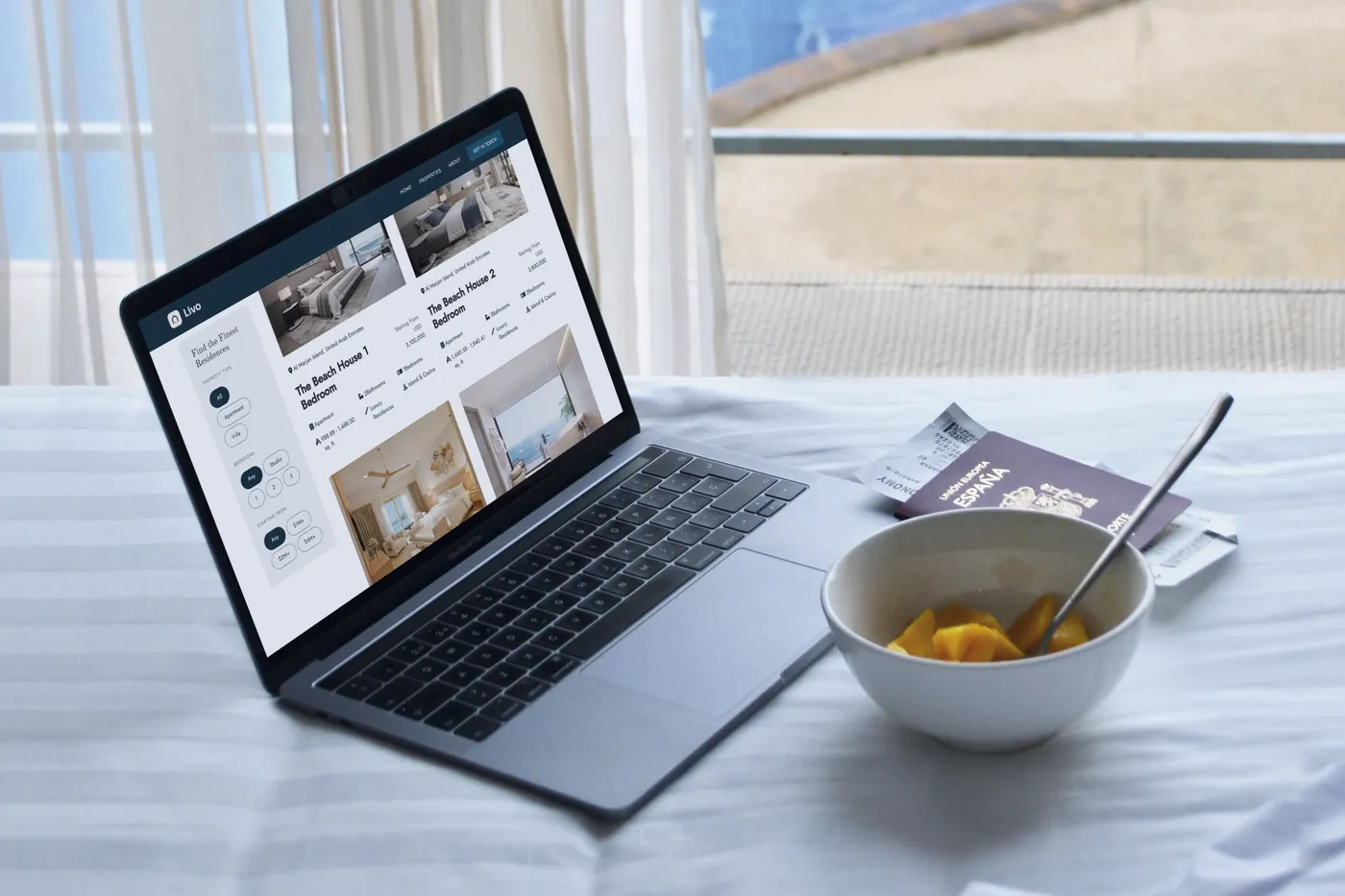The Livo concept's residences listing on a MacBook Pro on white bed linen by a window over a hotel pool.