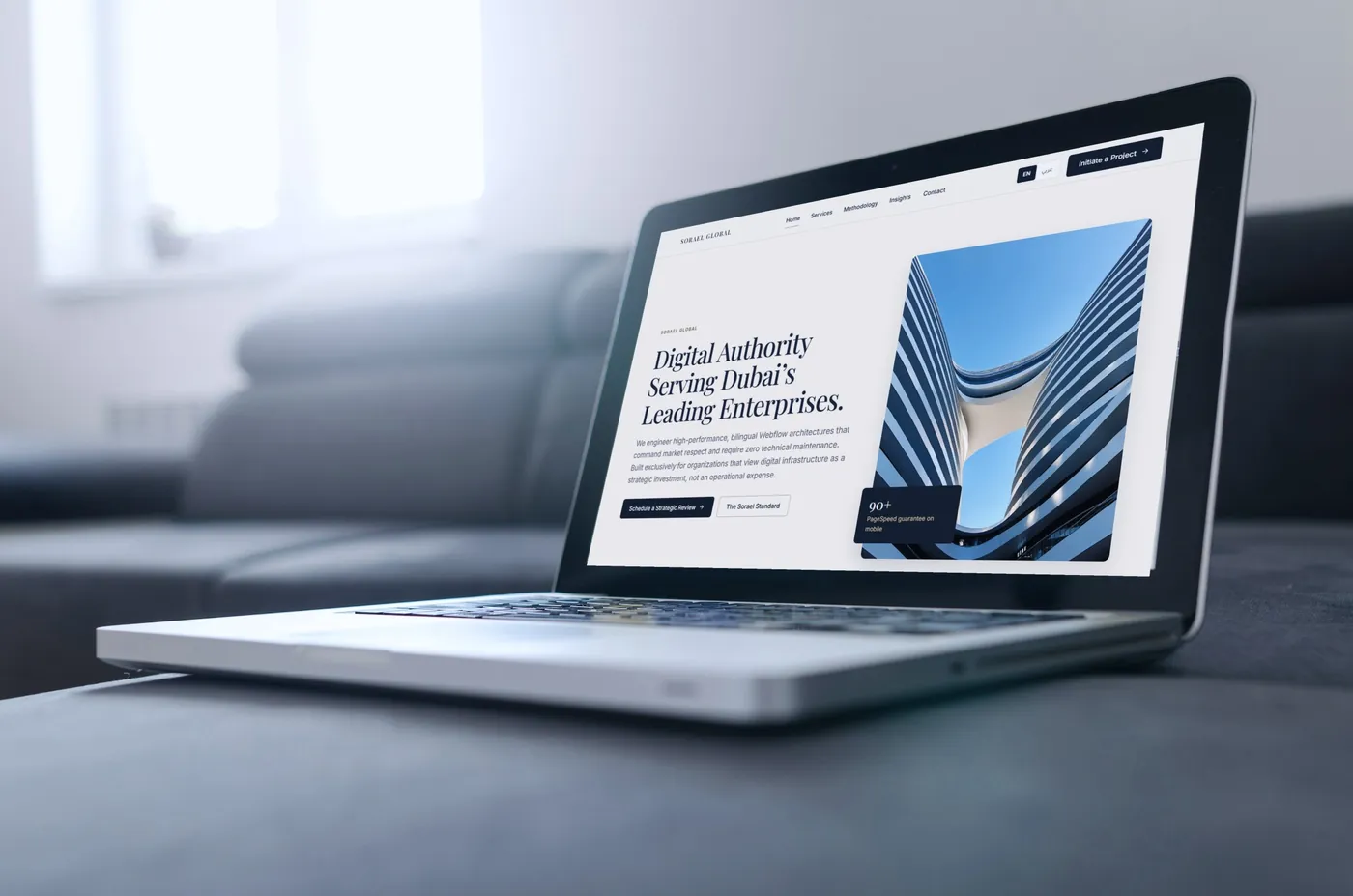 The Sorael Global English homepage on a laptop resting on a grey sofa.