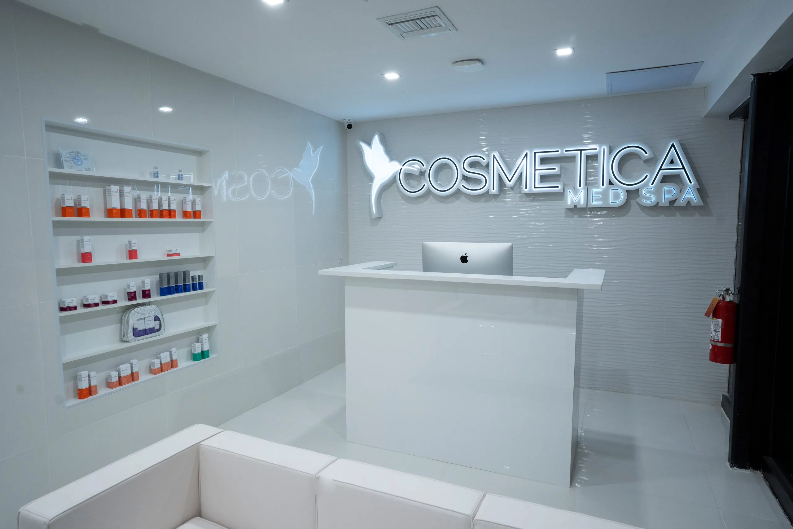 Reception area with built-in skin care shelves and white leather seating at Cosmetica Med Spa