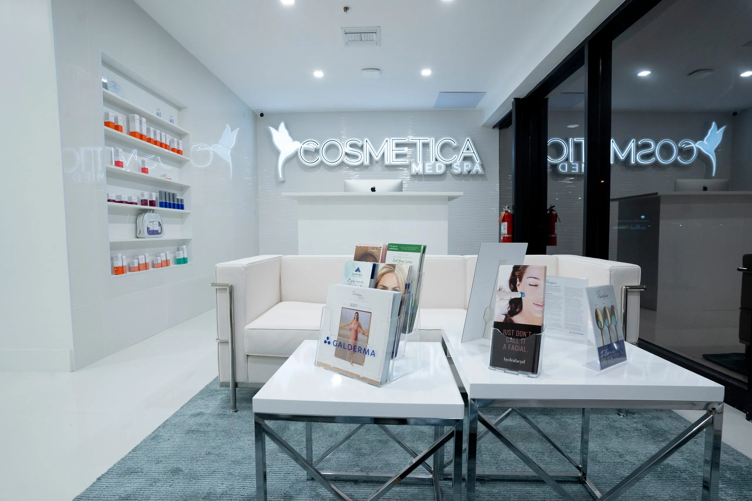White sofa and mirrored coffee tables displaying treatment brochures at Cosmetica Med Spa