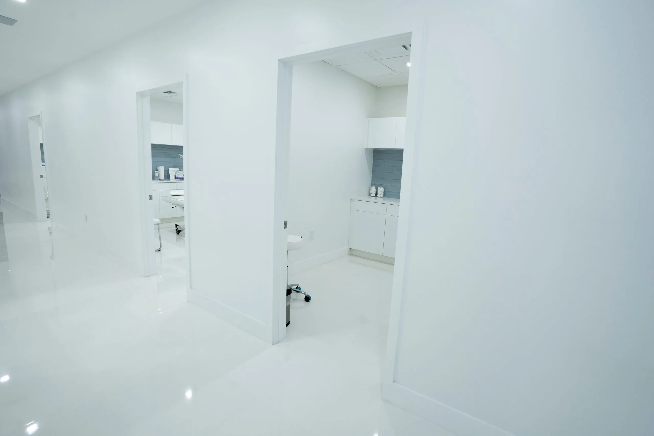 Open doorways into treatment rooms along a white hallway at Cosmetica Med Spa