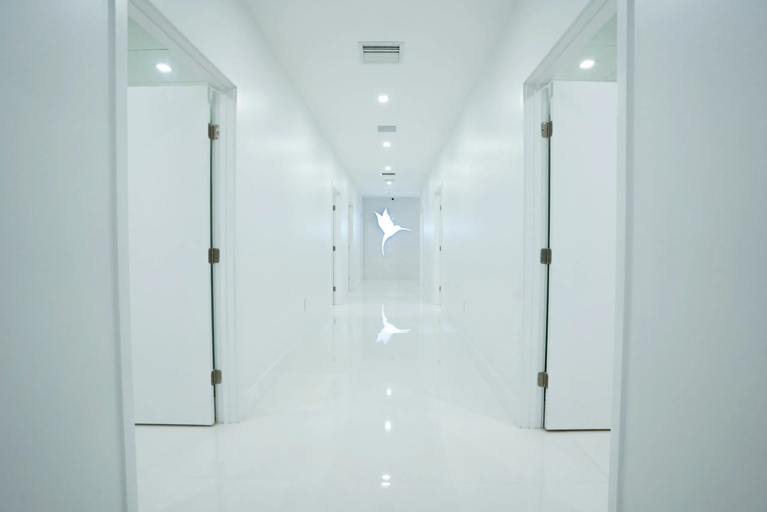 Symmetrical row of treatment room doors leading to the lit hummingbird logo at Cosmetica Med Spa