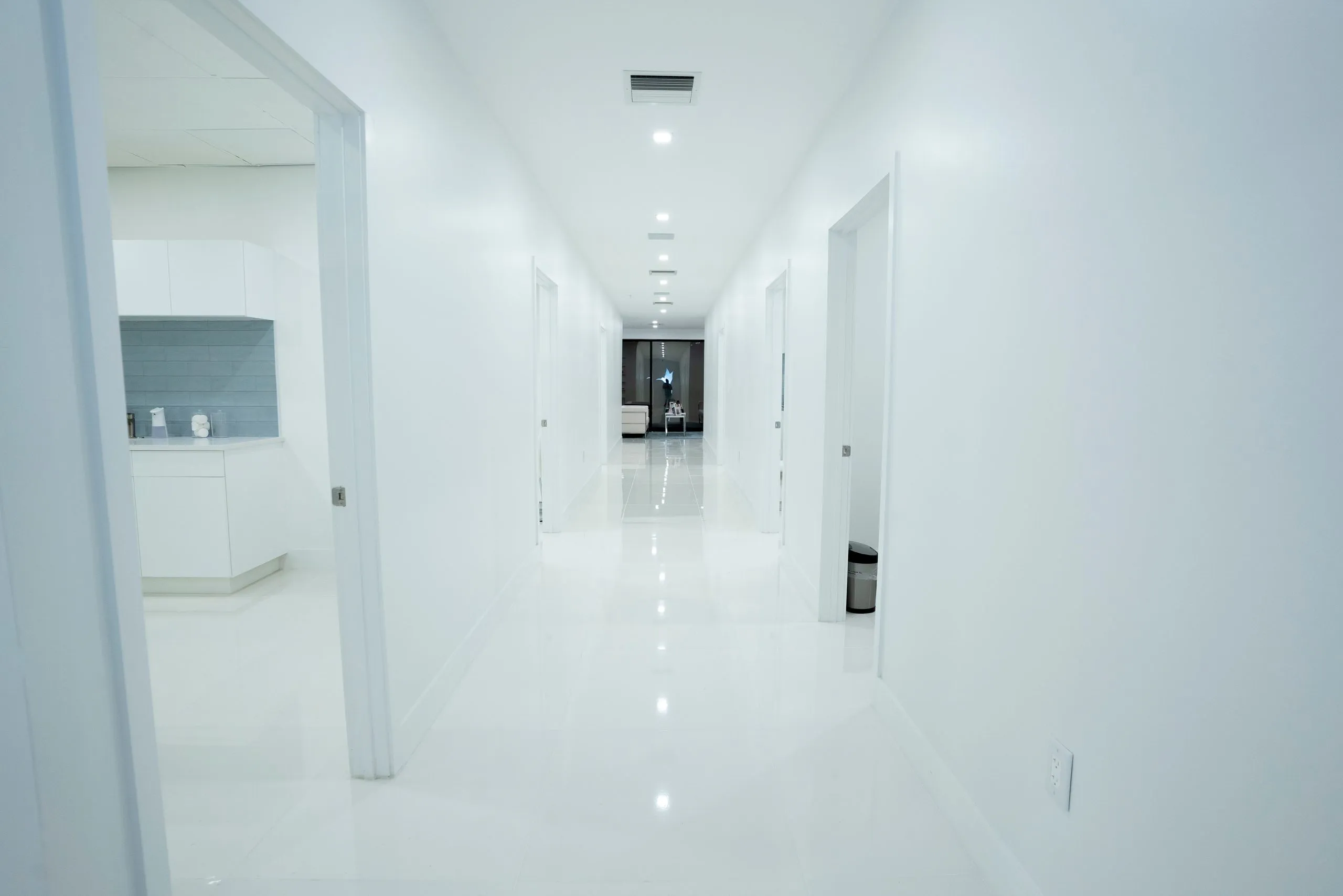 Hallway with an open cabinetry room on one side and the lobby ahead at Cosmetica Med Spa