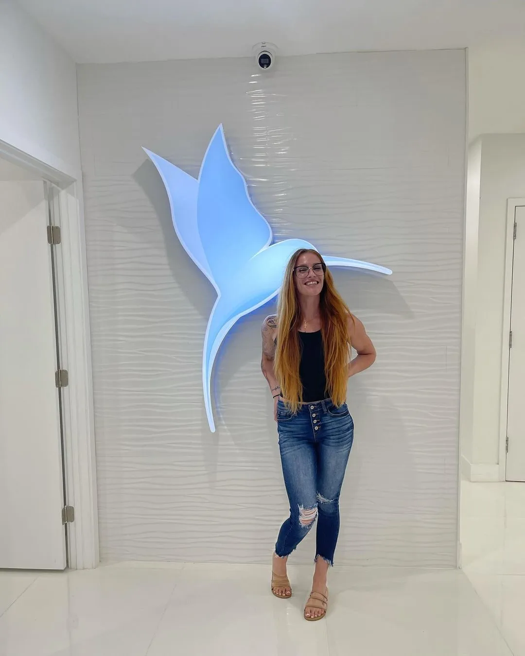 Smiling client in front of the hummingbird logo at Cosmetica Med Spa