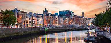 Evening skyline of Dublin with the River Liffey and Ha'penny Bridge under a colorful sky.