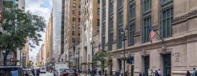 Busy city street lined with tall buildings and American flags on a partly cloudy day.