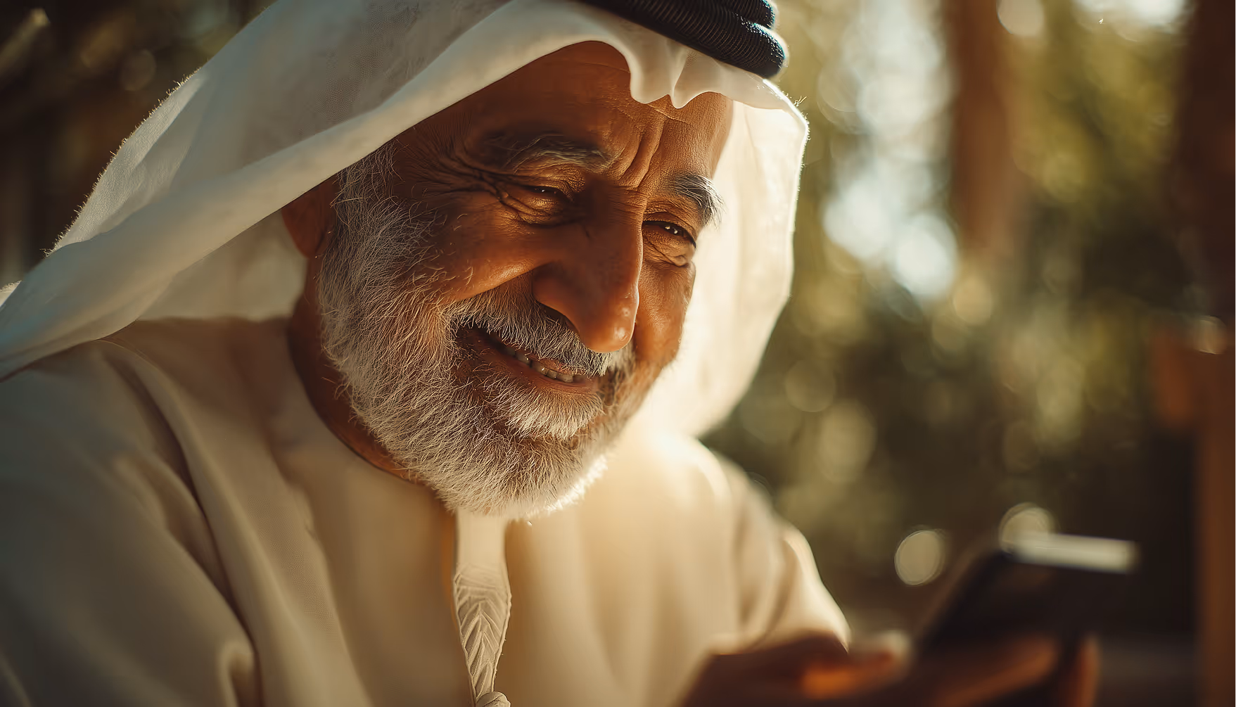 Smiling elderly man in traditional Middle Eastern attire looking at a smartphone outdoors.