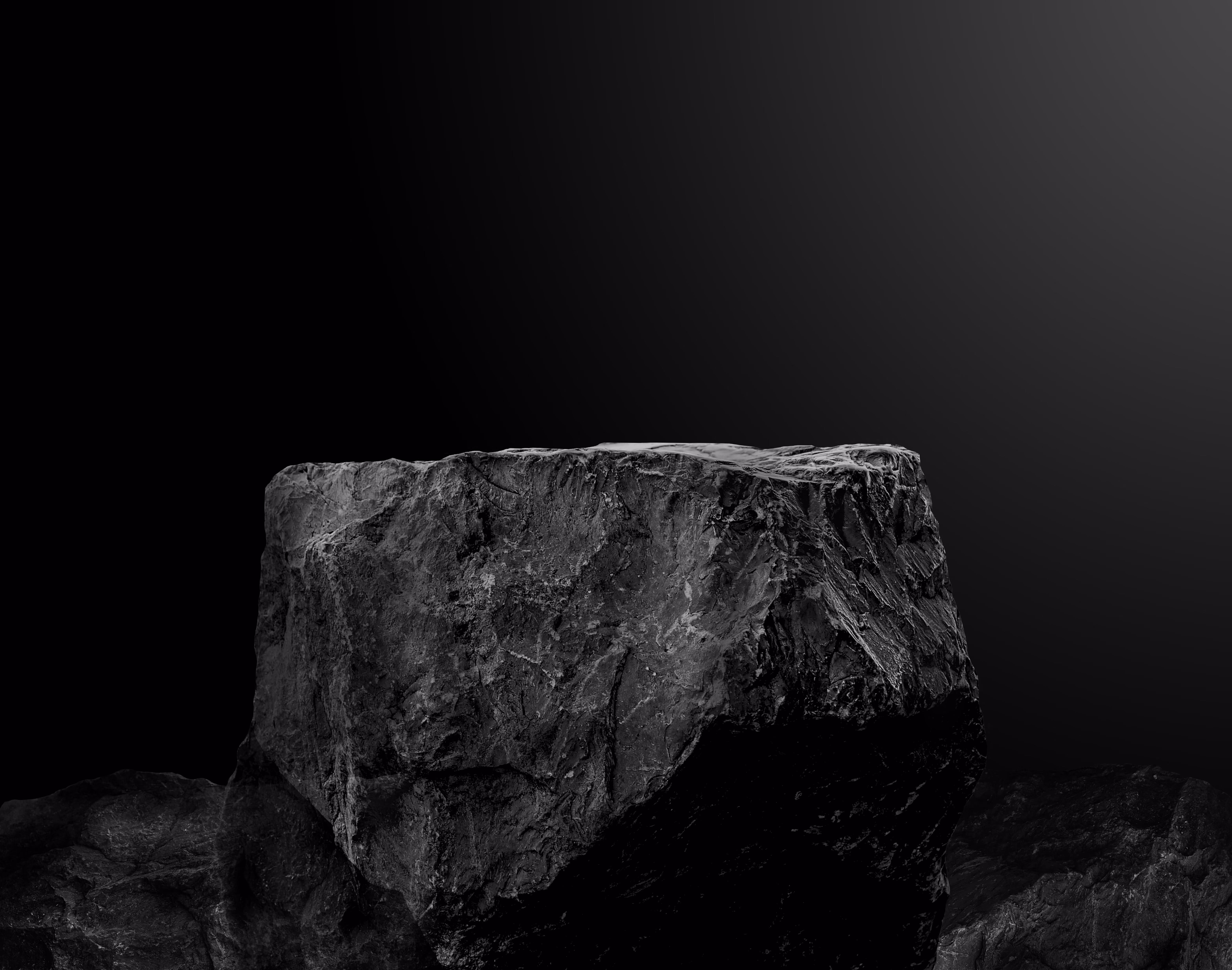 Close-up of a large black rock or stone with a rough, textured surface against a gradient dark background.