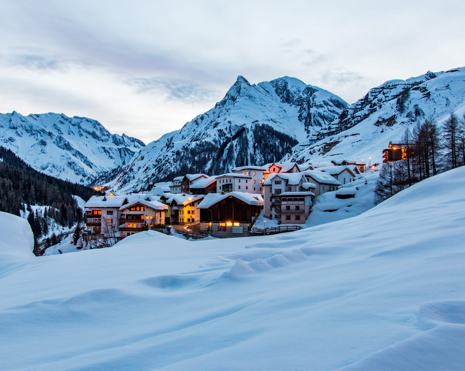 Verschneites Dorf Samnaun in der Abenddämmerung vor den Gipfeln der Silvretta