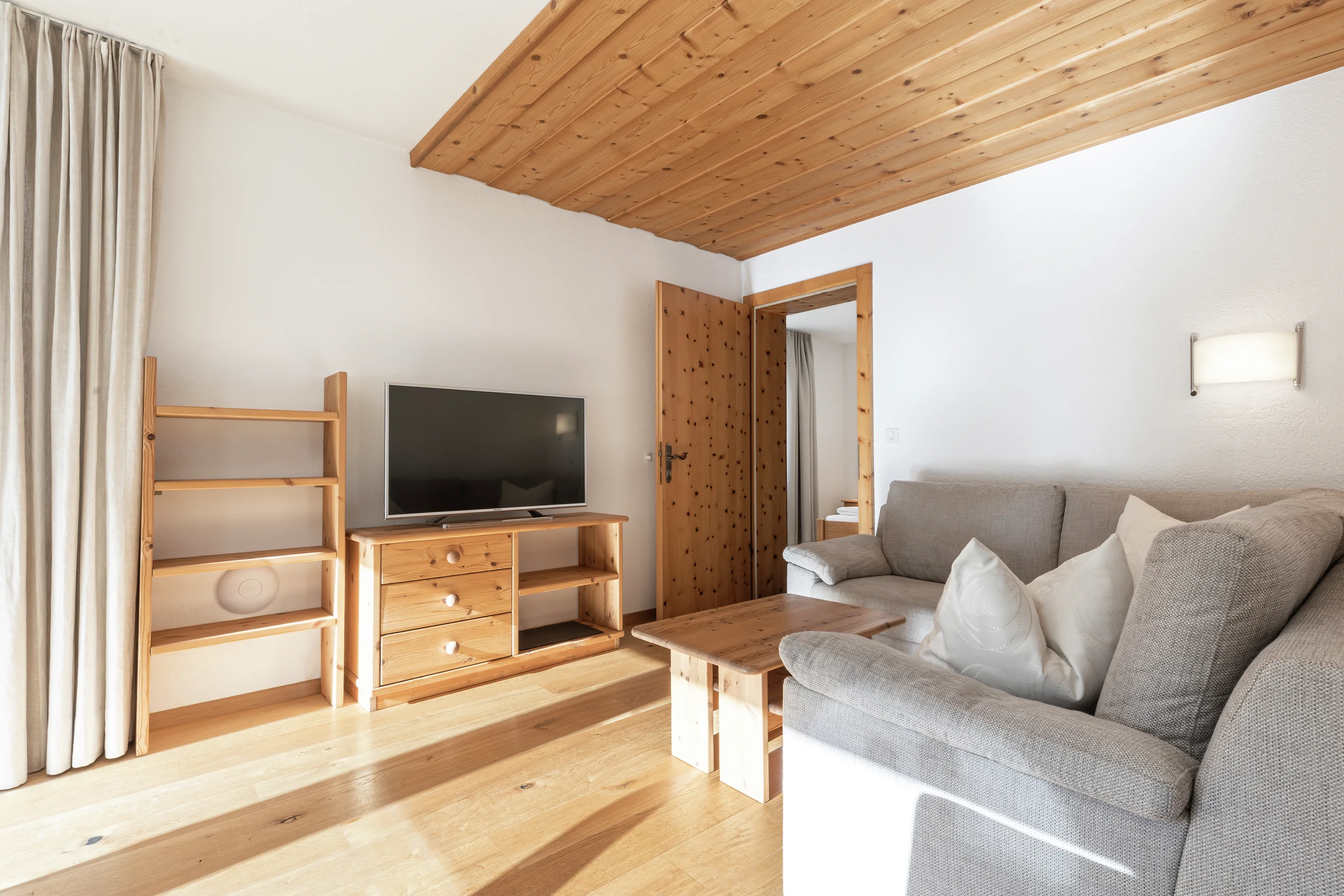 Wohnbereich mit grauem Sofa, Fernseher und Holzdecke, Wohnung 202