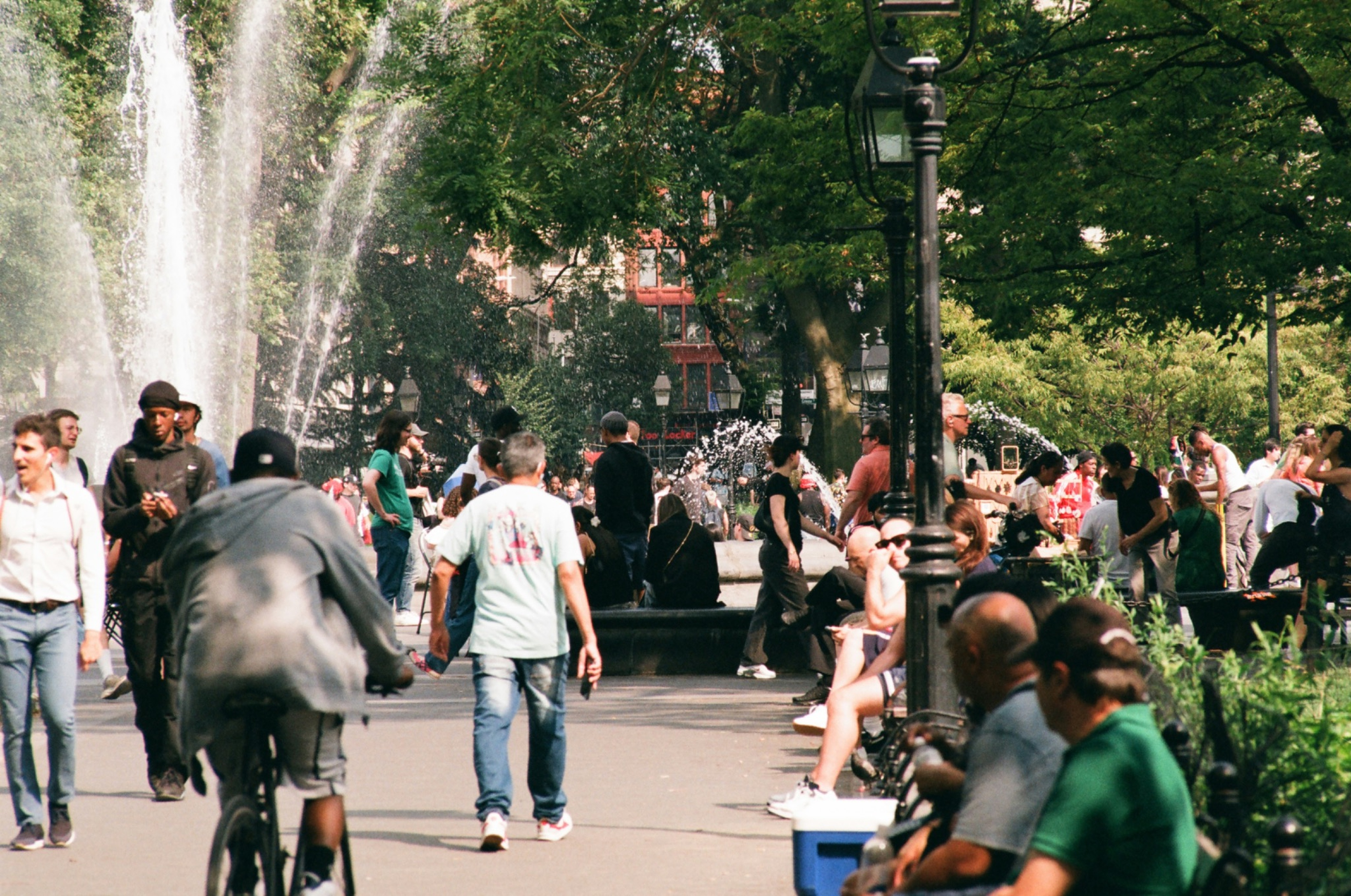 People walking, cycling and gathering near a fountain in a leafy New York City park