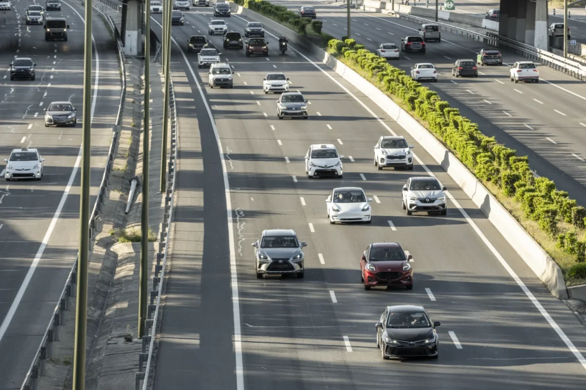 Cars moving along a wide multi-lane highway lined with green hedges