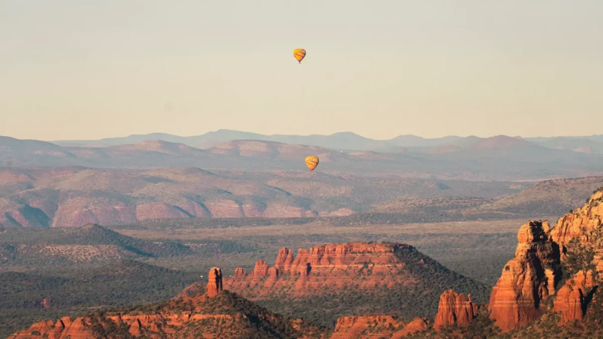 Two hot air balloons drifting over red rock formations at sunrise