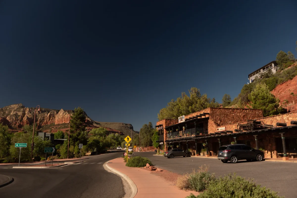 Shops along a curving road with red rocks under a dusk sky