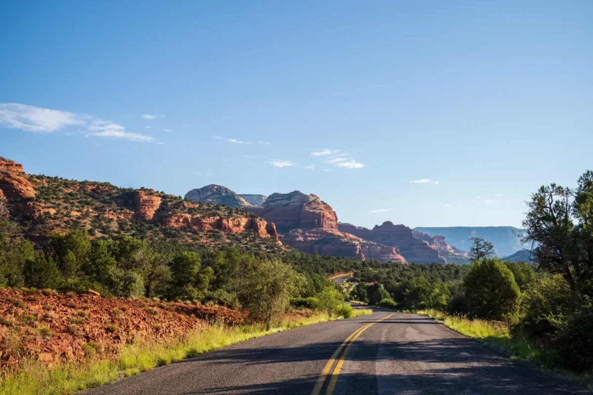 Two-lane road leading toward red rock buttes on a sunny day