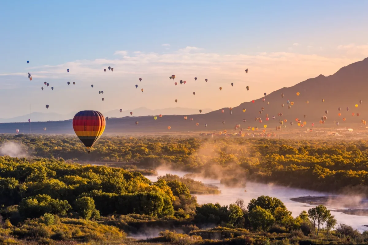 Dozens of hot air balloons rising over a misty river valley