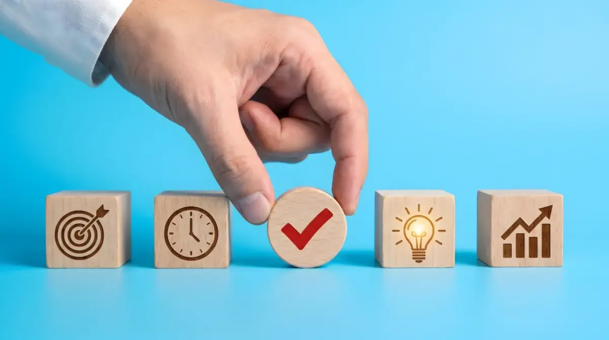 Hand placing a red checkmark block among wooden blocks with planning icons
