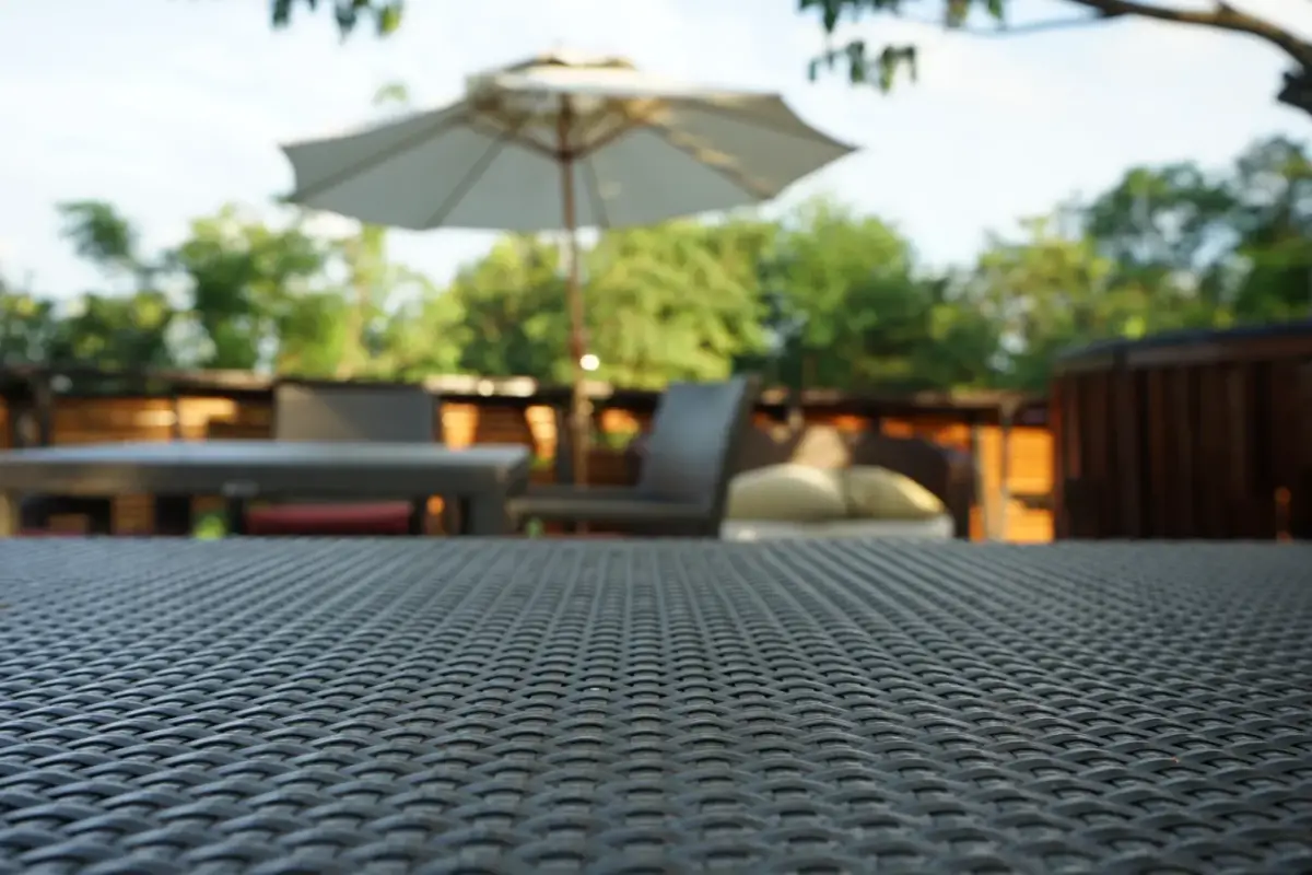 Wicker patio table in the foreground with an umbrella and chairs blurred behind