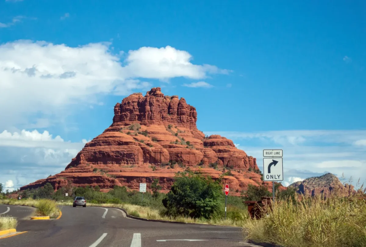 Bell Rock towering over a curving highway under a blue sky with white clouds