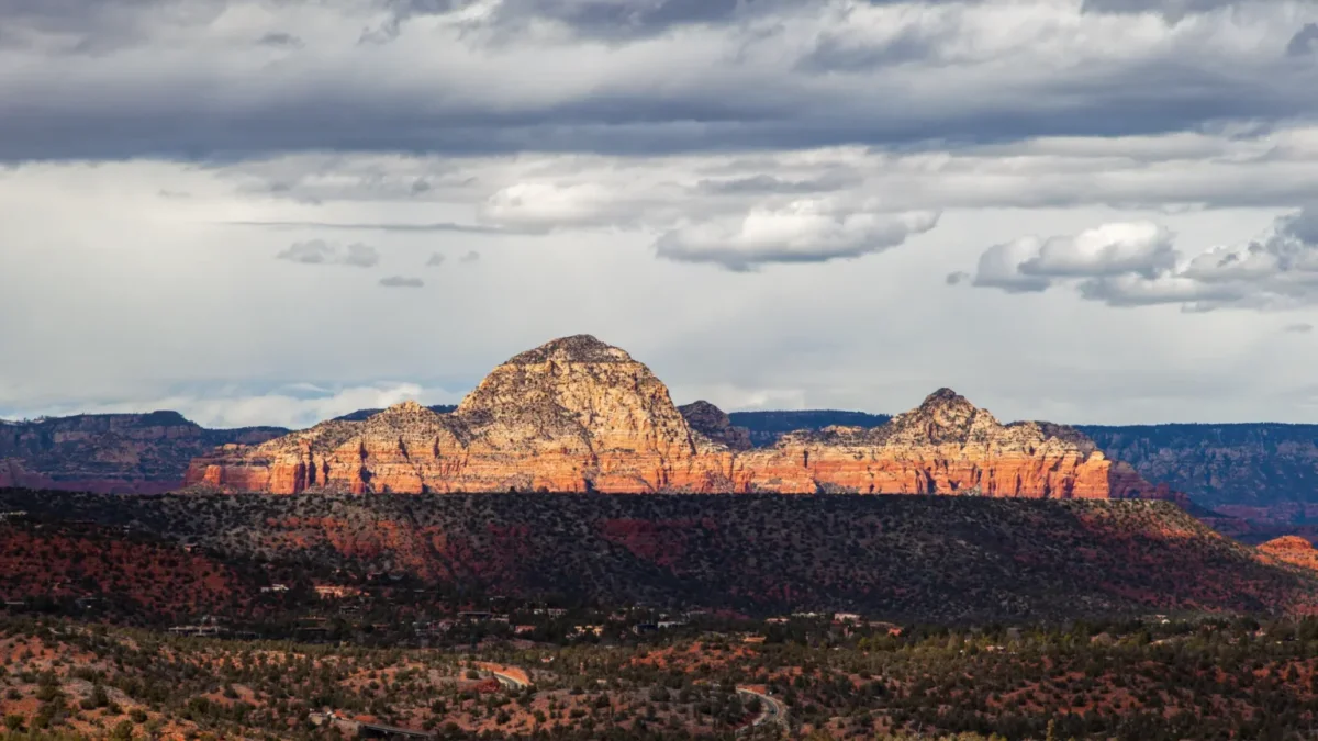 Sunlit red rock peaks beneath a gray cloud-covered sky