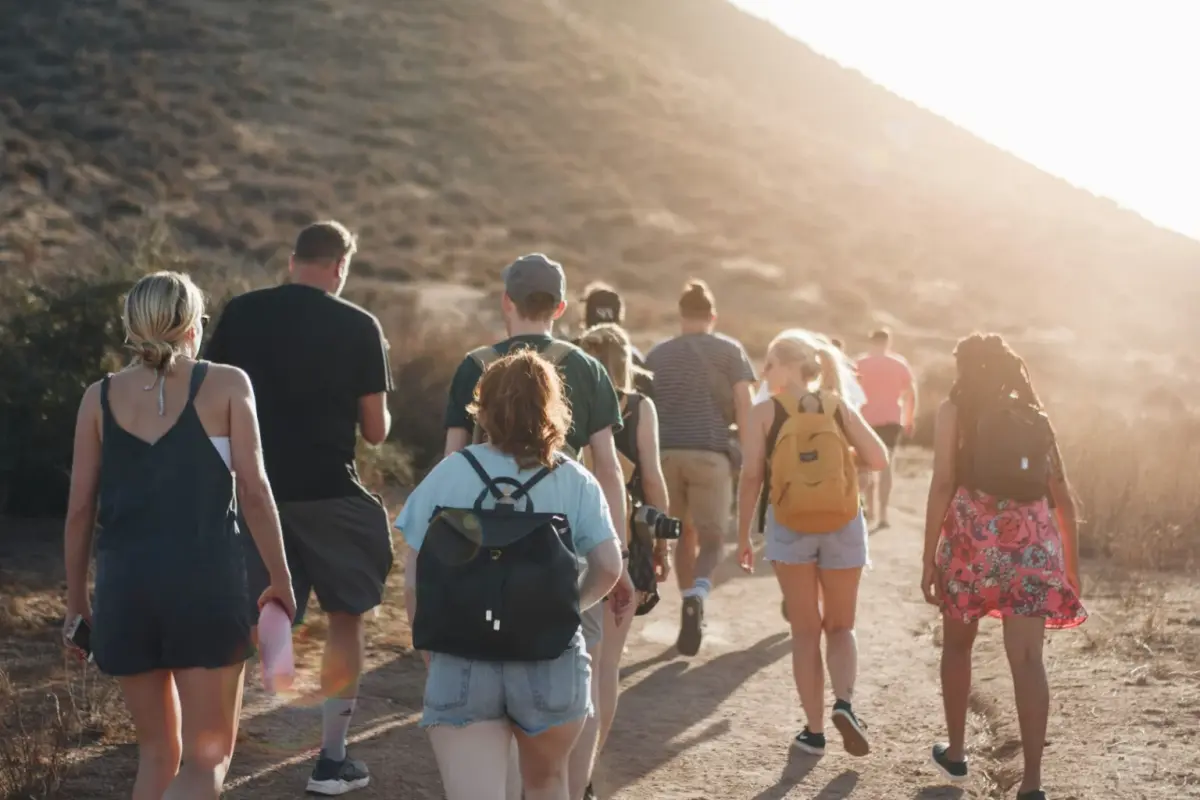 Group of friends hiking up a dusty hillside trail in warm evening light
