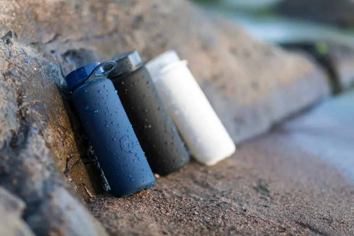 Three reusable water bottles in blue, black and white leaning against a rock