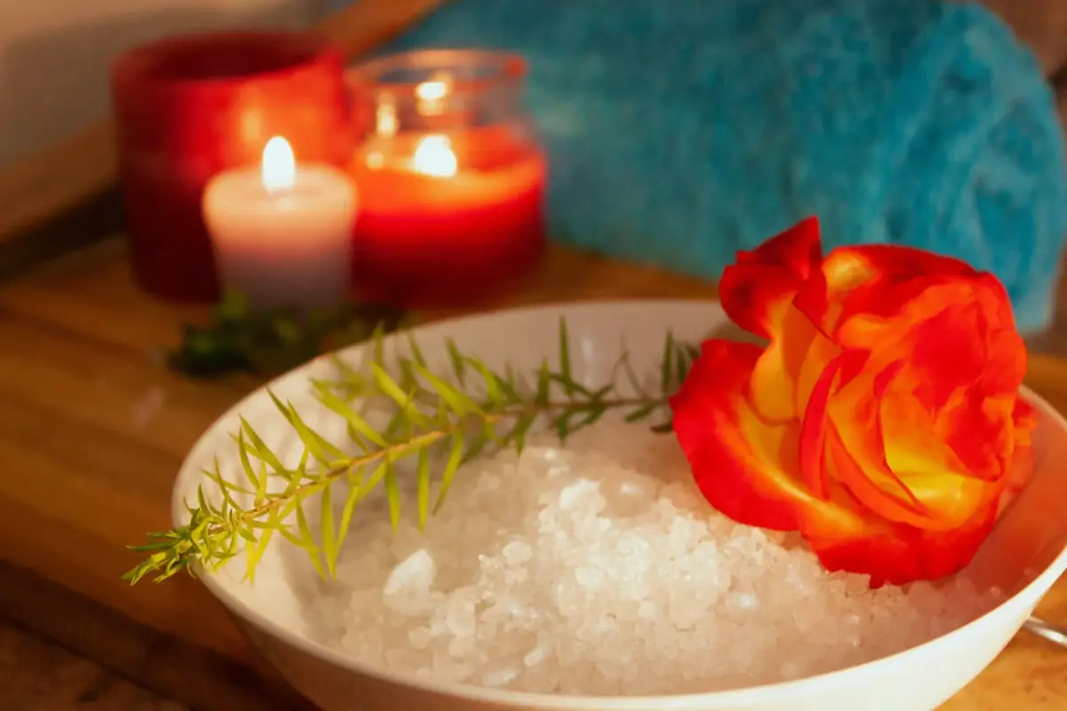 Bowl of bath salts with an orange rose and lit candles in the background