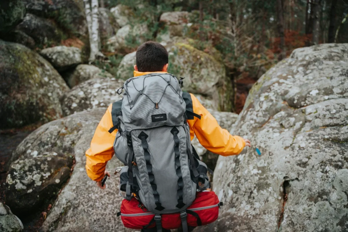 Hiker in an orange jacket with a gray backpack walking among large boulders