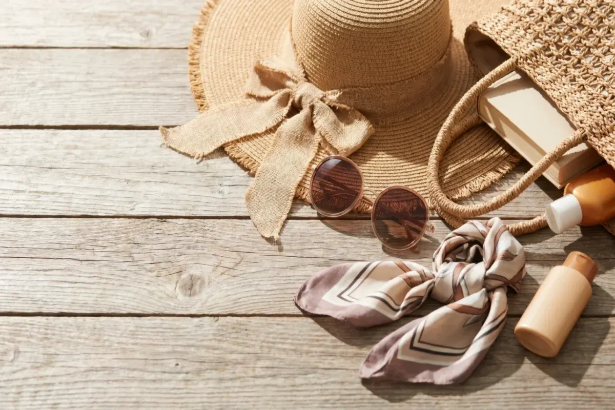 Straw sun hat, sunglasses, scarf and sunscreen bottles on wooden boards