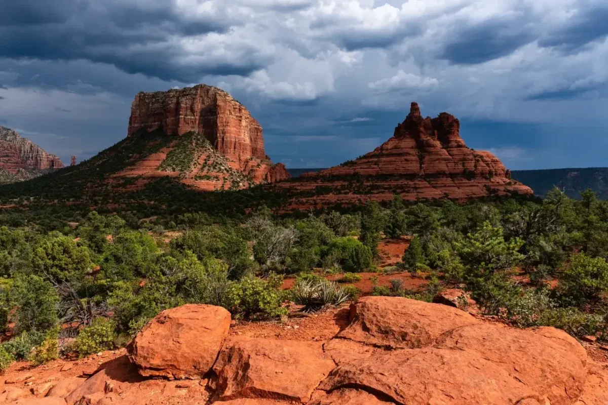 Courthouse Butte and Bell Rock beneath dark storm clouds above green desert brush