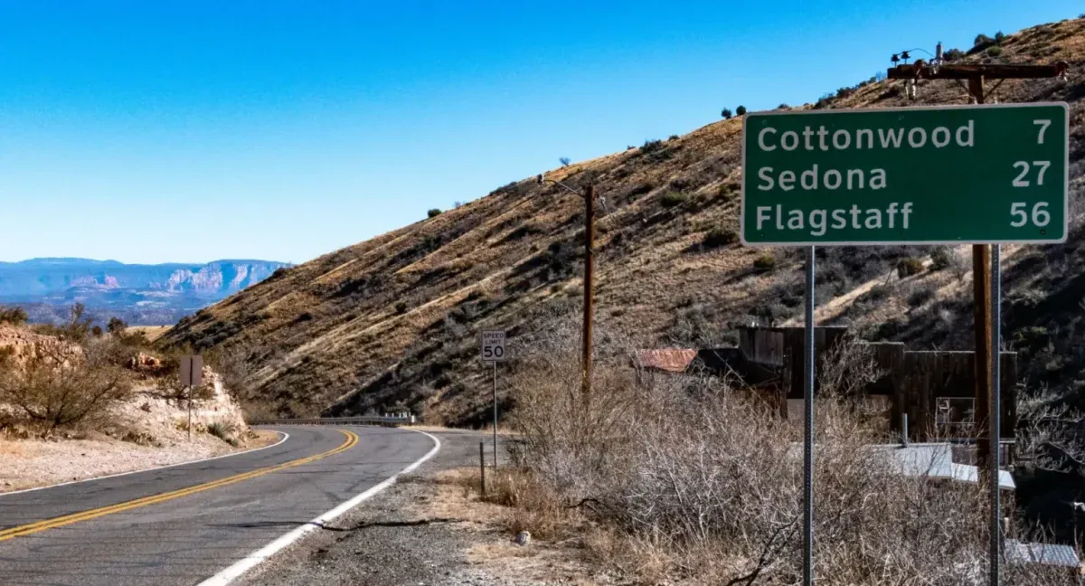 Highway sign listing distances to Cottonwood, Sedona and Flagstaff on a mountain road