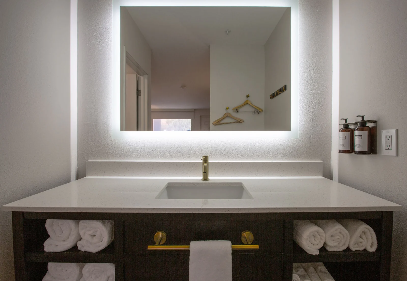 Bathroom vanity viewed straight-on, with towels on both sides of the sink and the mirror reflecting the hallway.