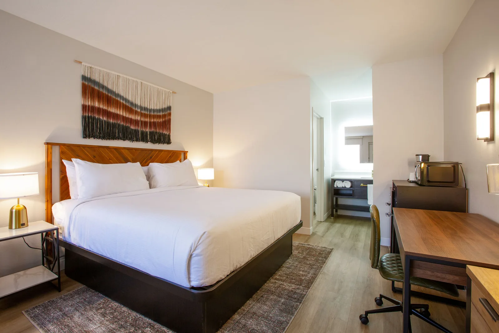 King bed with a woven wall hanging, viewed toward the hallway and bathroom.