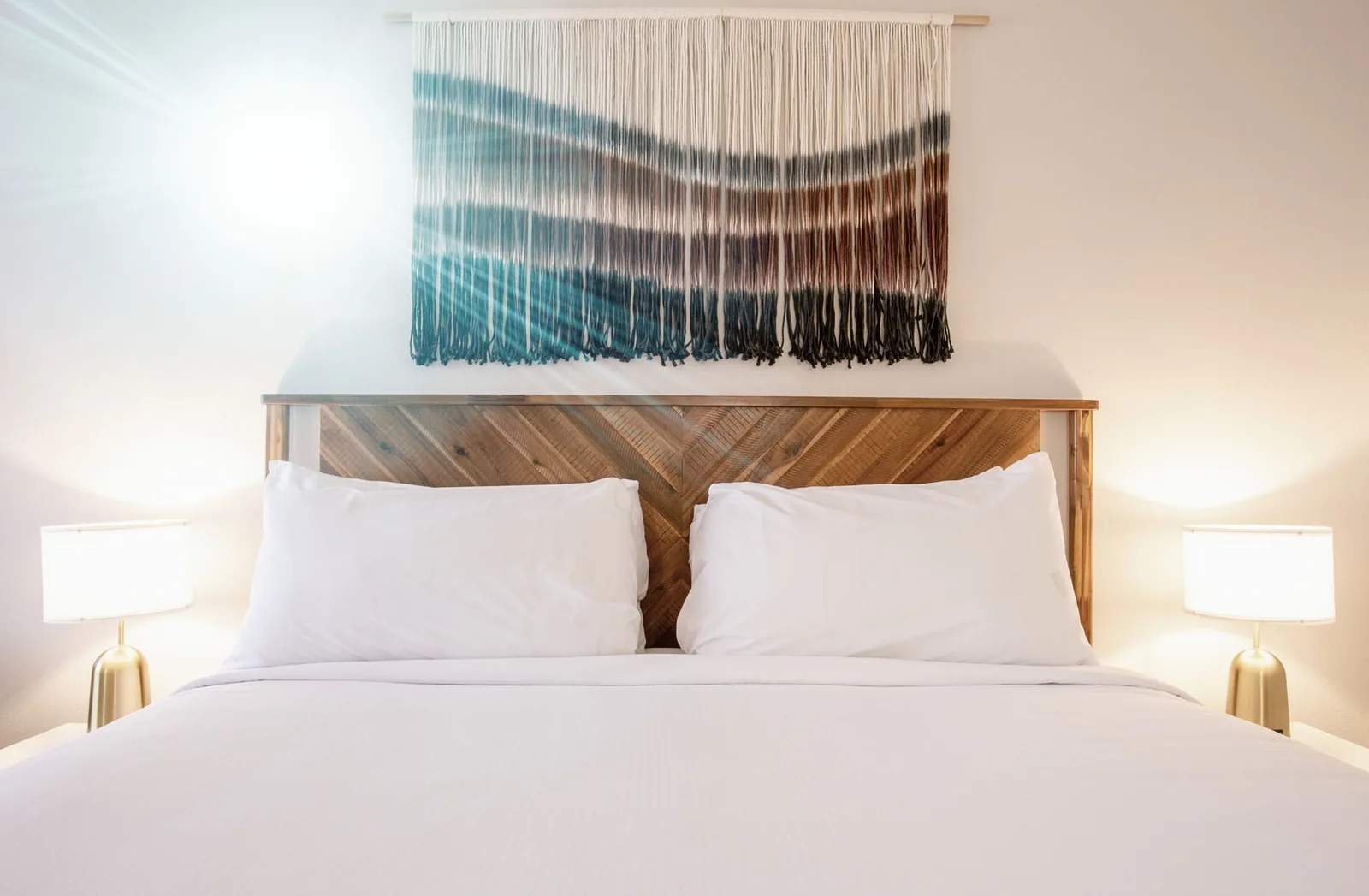 Close view of the king bed's pillows and headboard with the woven wall hanging above.