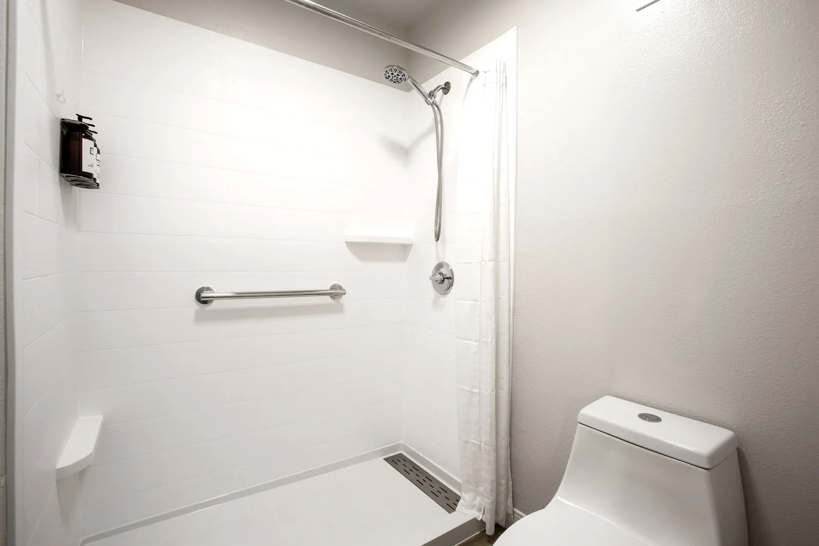 Accessible bathroom with a roll-in shower, grab bar, and adjacent toilet.