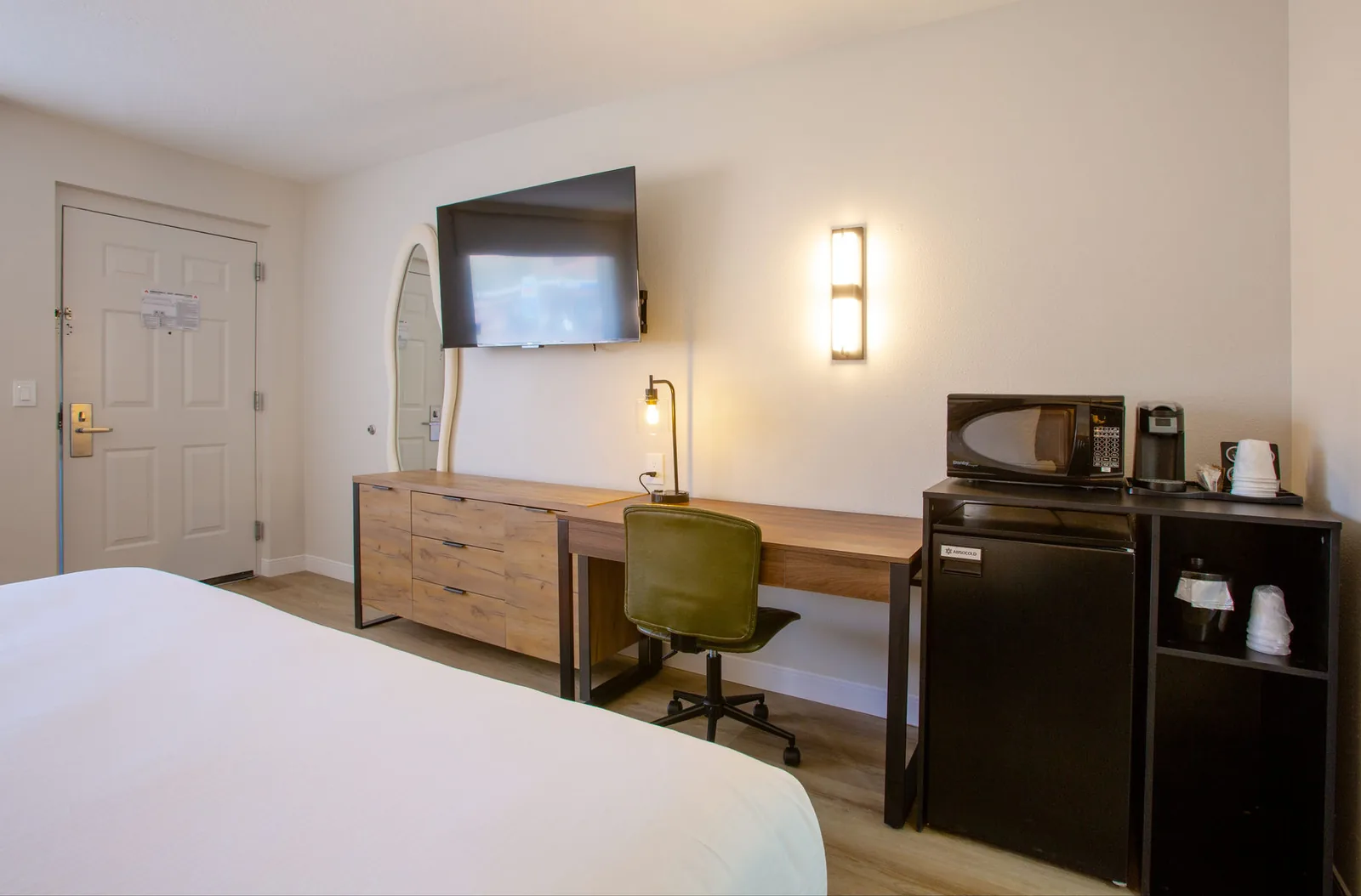 Room view from the door toward the desk, TV, and mini fridge, with the bed at the edge of frame.