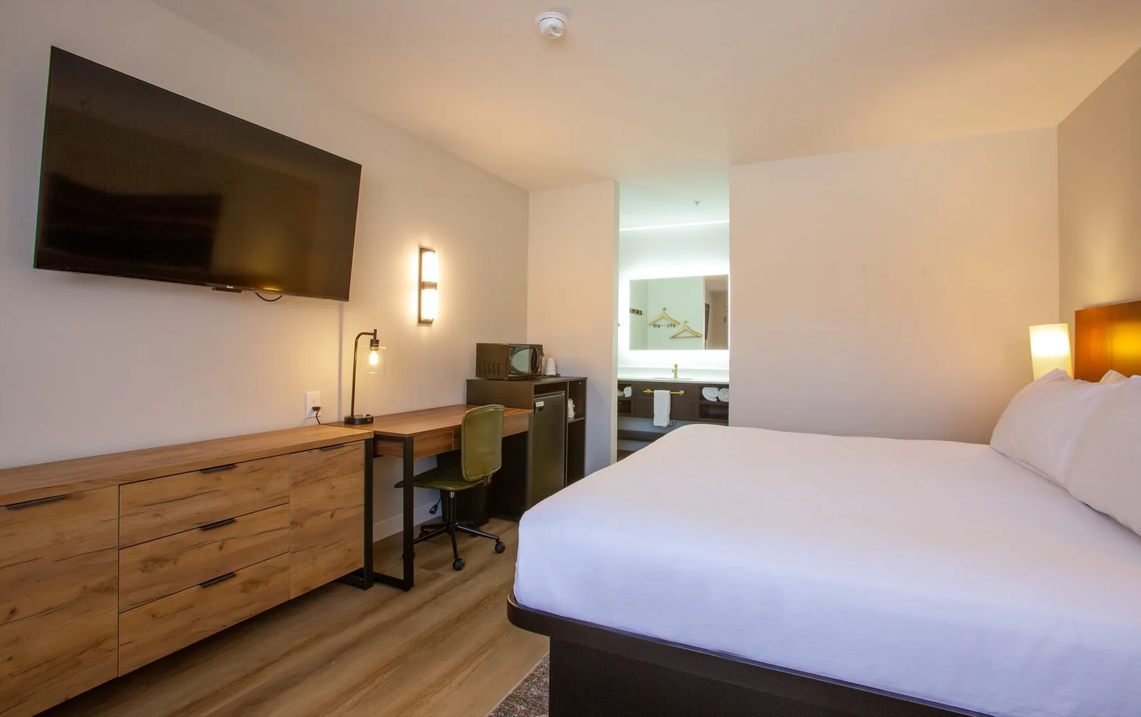 Desk and wall-mounted TV beside an oval mirror, with the foot of the bed in view.
