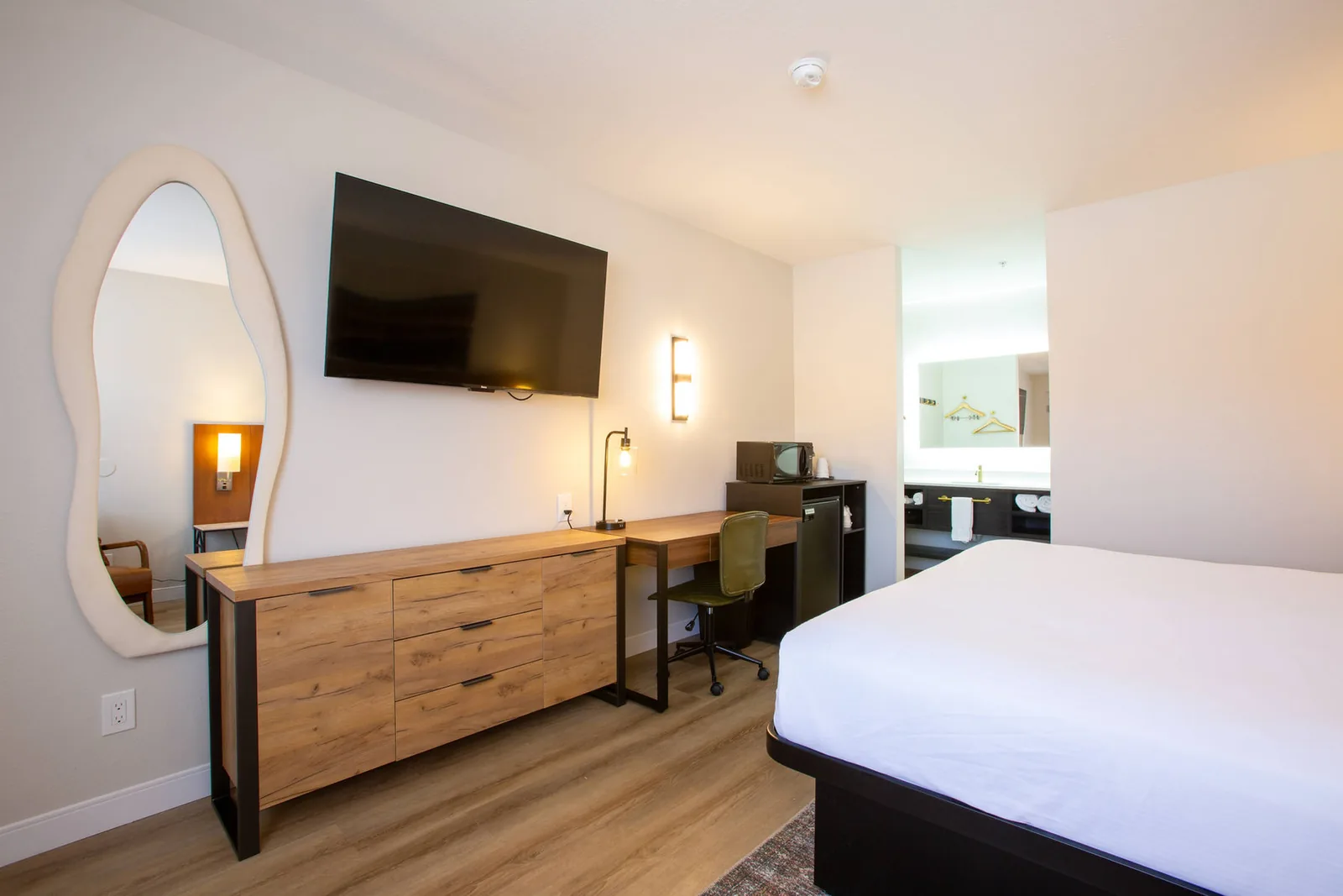 Oval mirror, dresser, and wall-mounted TV along the desk wall opposite the bed.