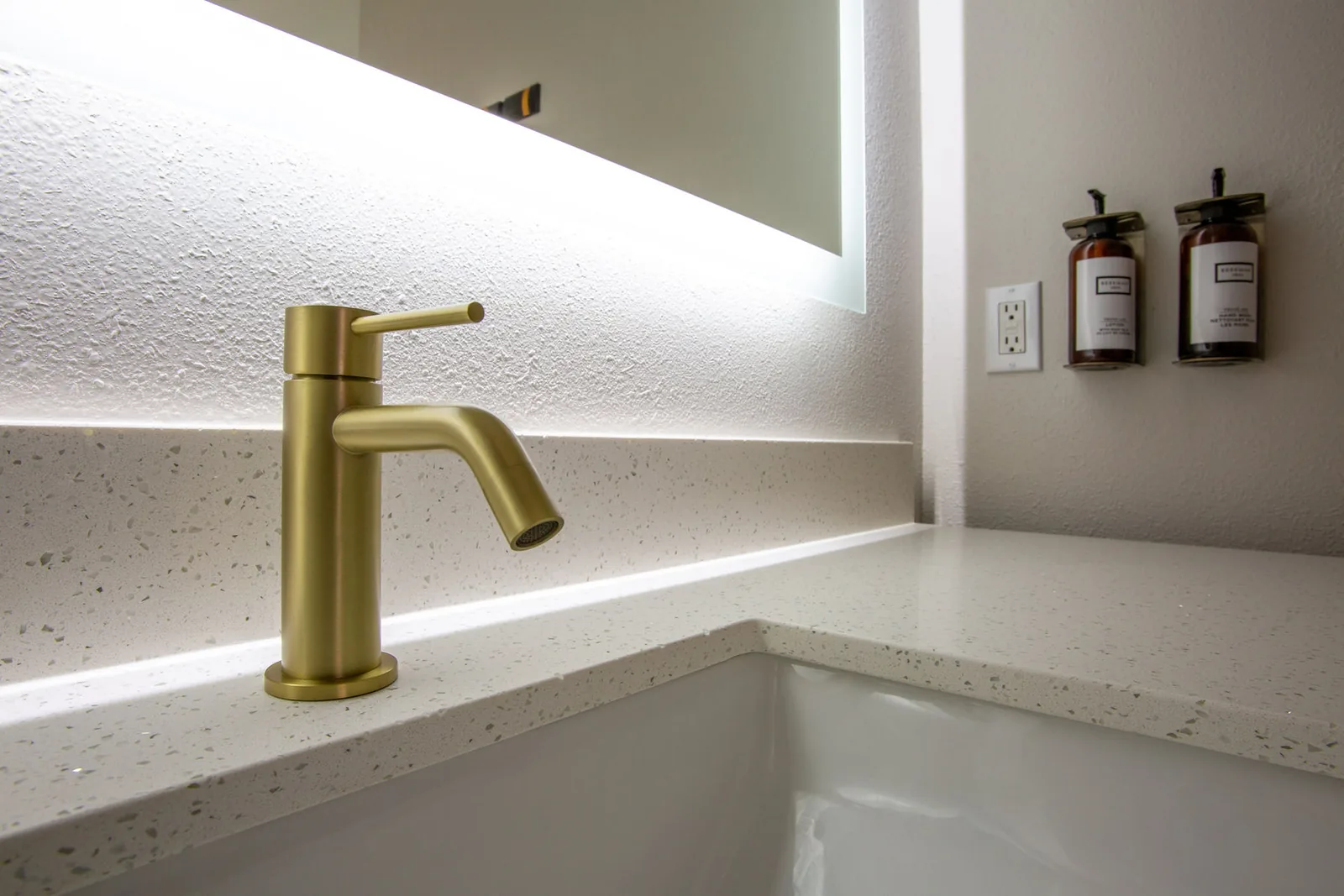 Close view of the gold bathroom faucet on the white stone countertop.
