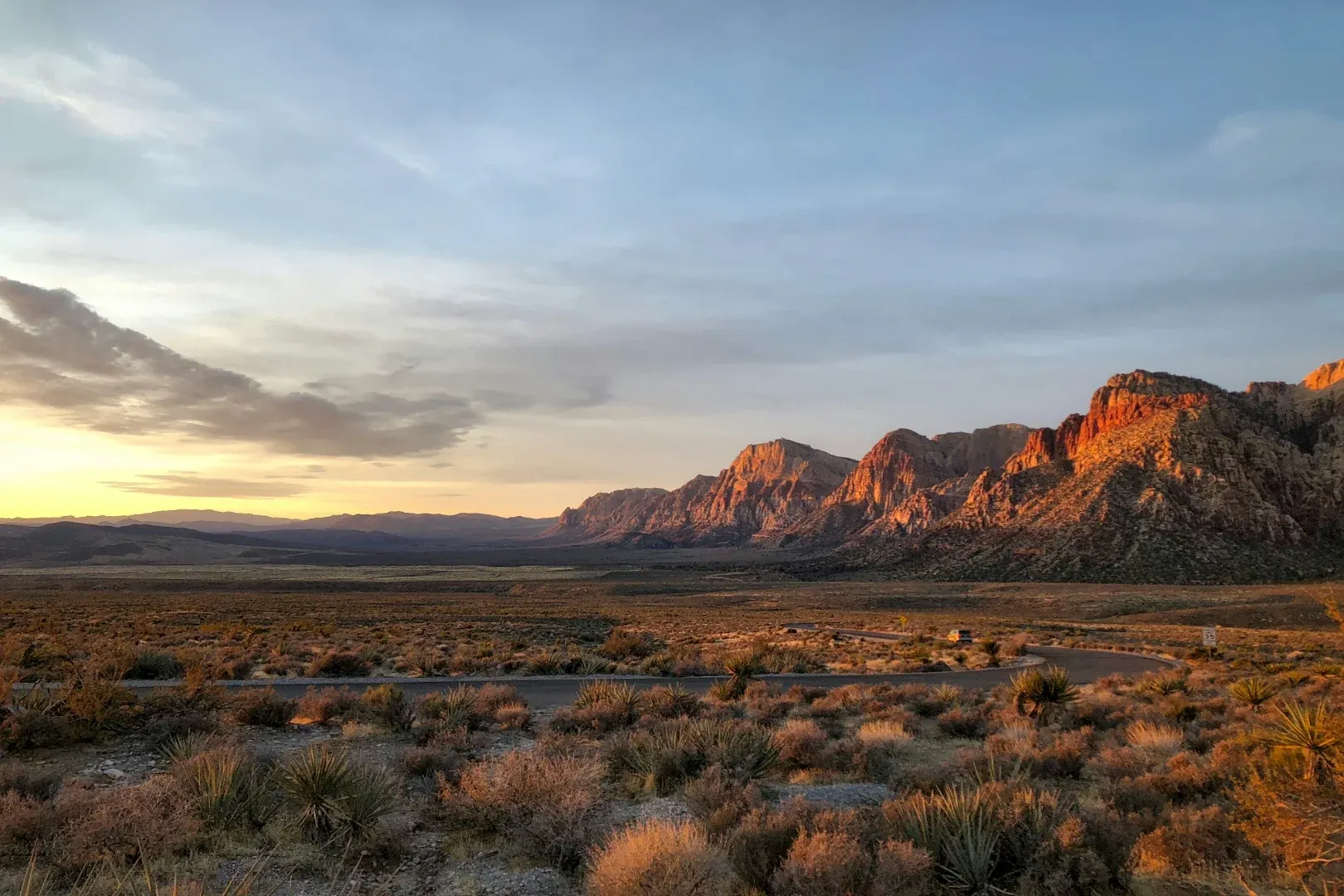 Red rock desert valley at dusk with layered mountain silhouettes and a dirt road below.