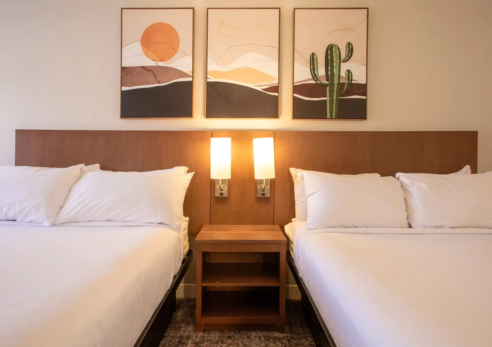 Close view of the two queen beds with a shared nightstand and lit wall sconces between them.