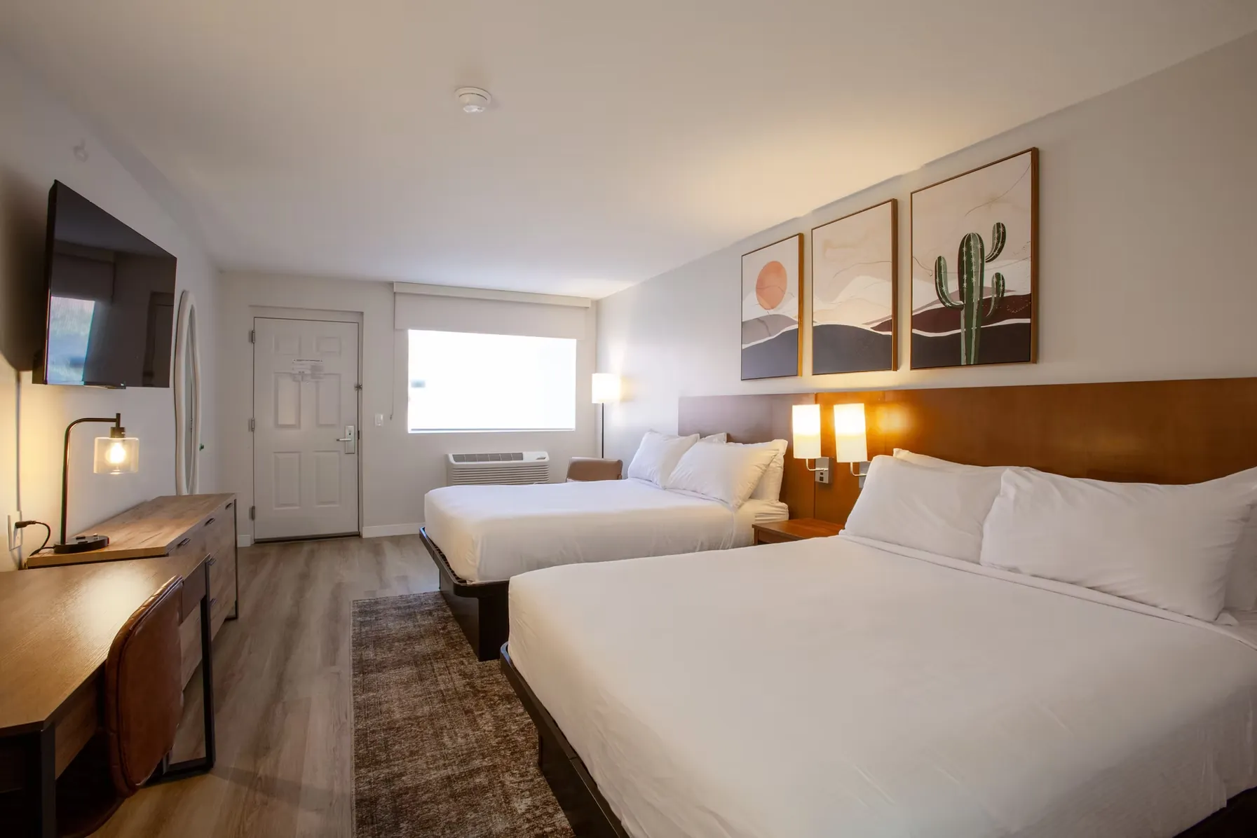 Queen beds viewed from the entry, with the desk and lamp on one side and the window on the other.