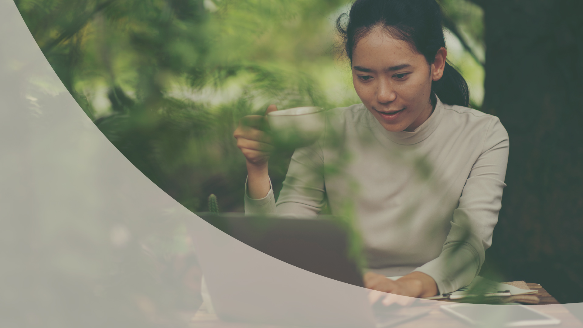 Woman smiling at a laptop among green leaves