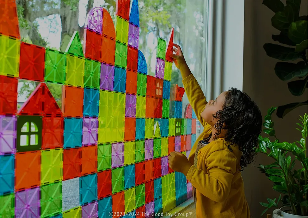 Child building a colorful Magna-Tiles wall against a window