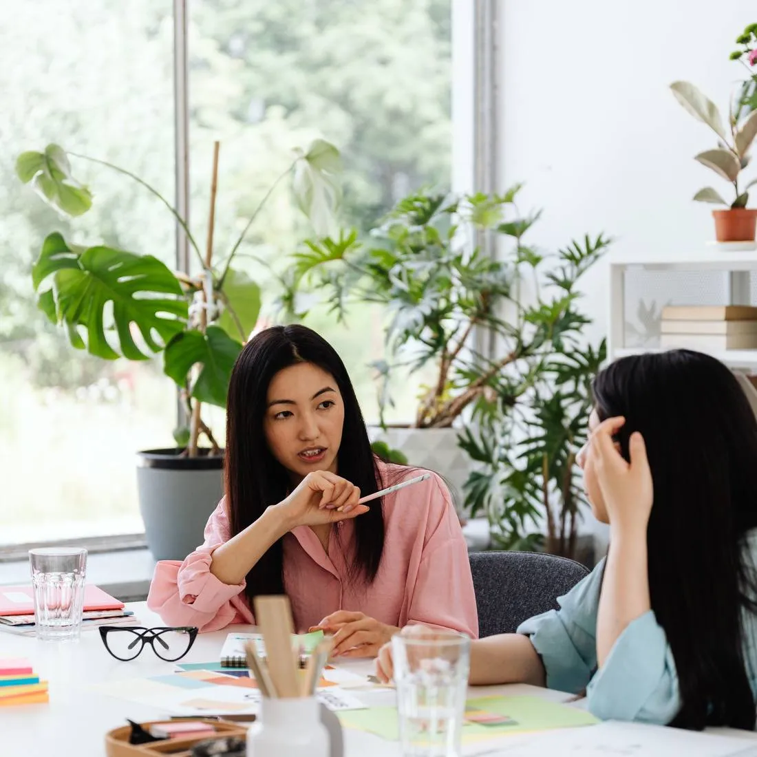 Two colleagues talking at a desk in a plant-filled workspace