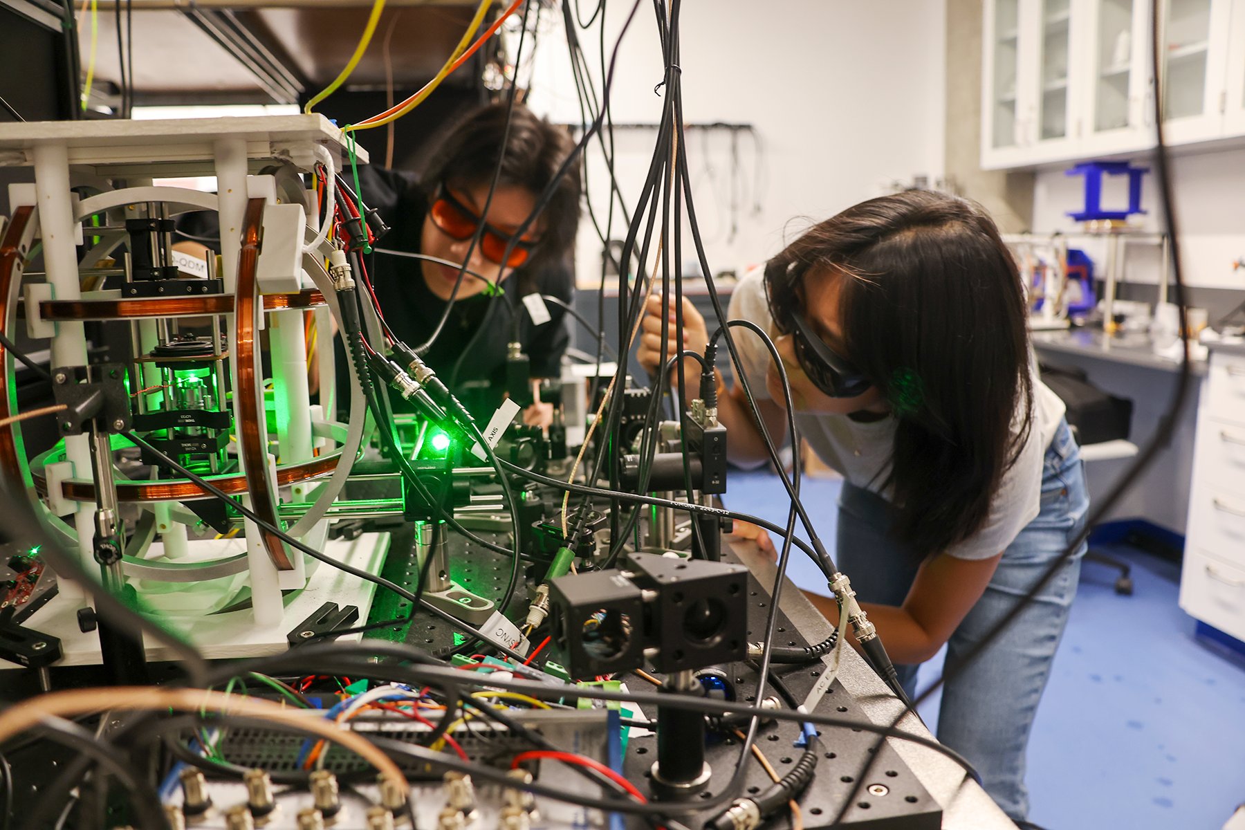 Two researchers wearing safety glasses work with laser optics equipment in a lab