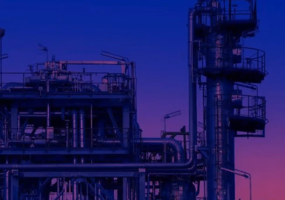 Industrial plant structure with pipes, platforms, and railings silhouetted against a twilight sky with shades of blue and purple.