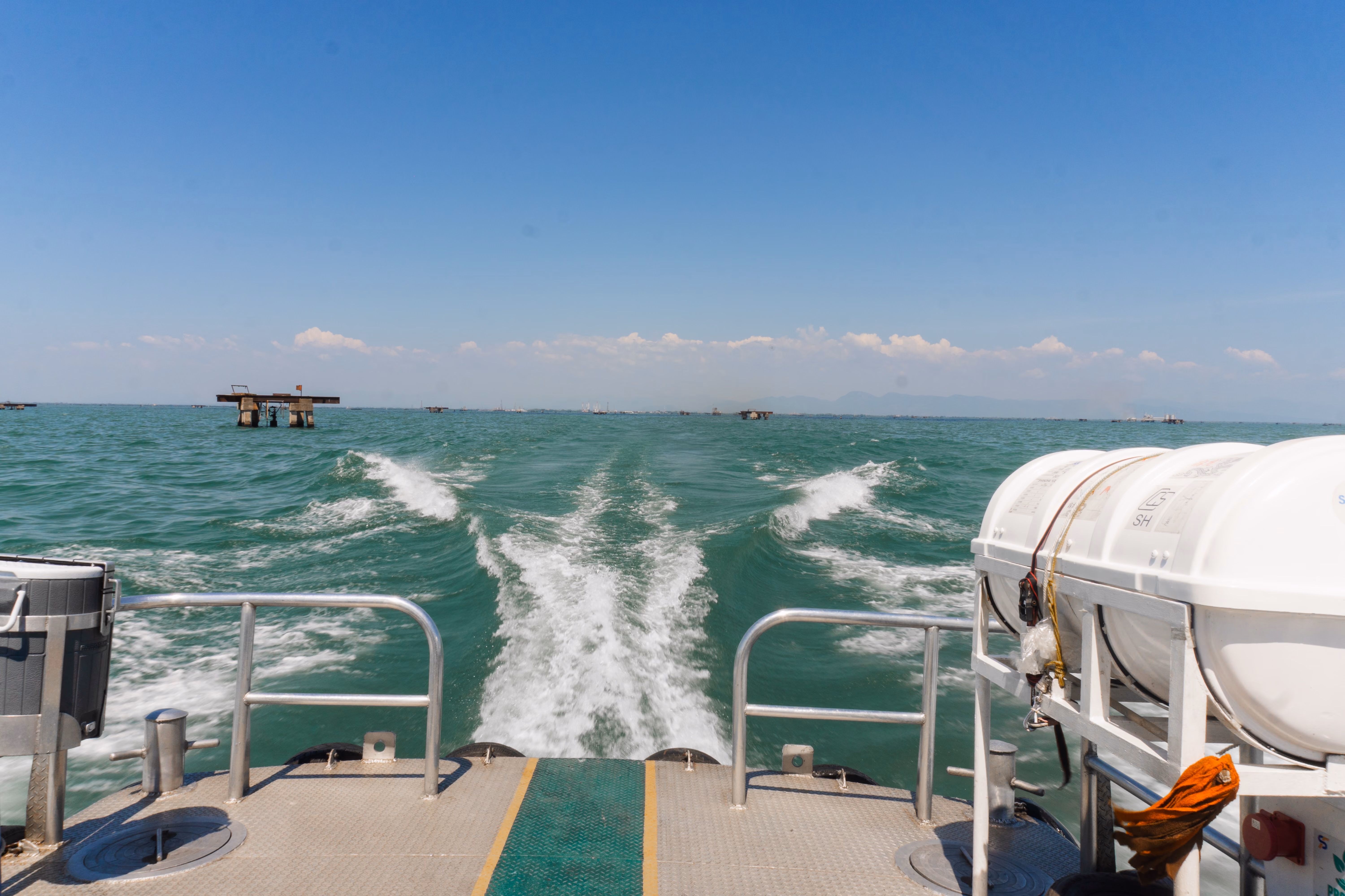View from the stern of a crew boat crossing open water toward distant offshore platforms