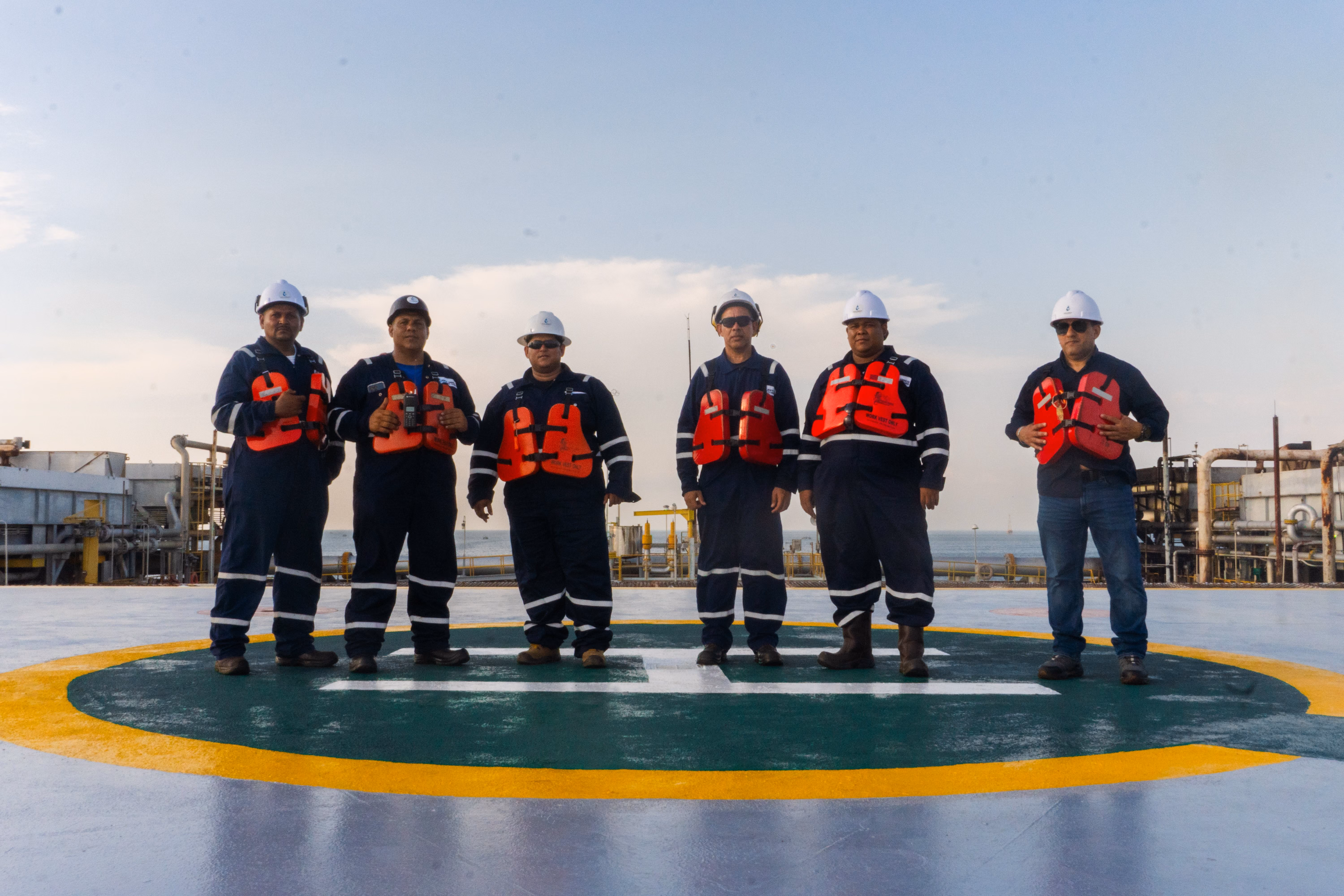 Six crew members in hard hats and life vests standing on an offshore helipad
