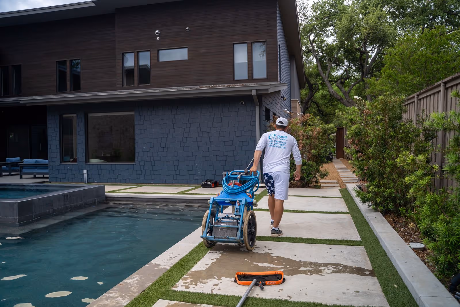 CK Pools technician transporting maintenance equipment beside a modern residential pool